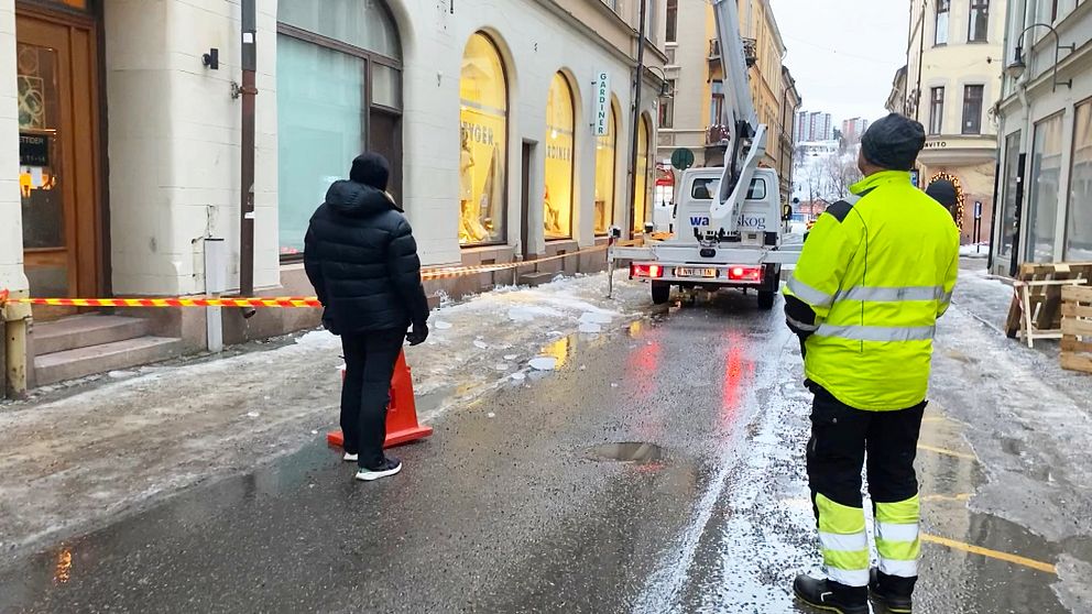 I centrala Sundsvall där det fallit ner stora isbitar från taket. På bilden står personer och tittar upp på en skylift som tar bort istapparna.