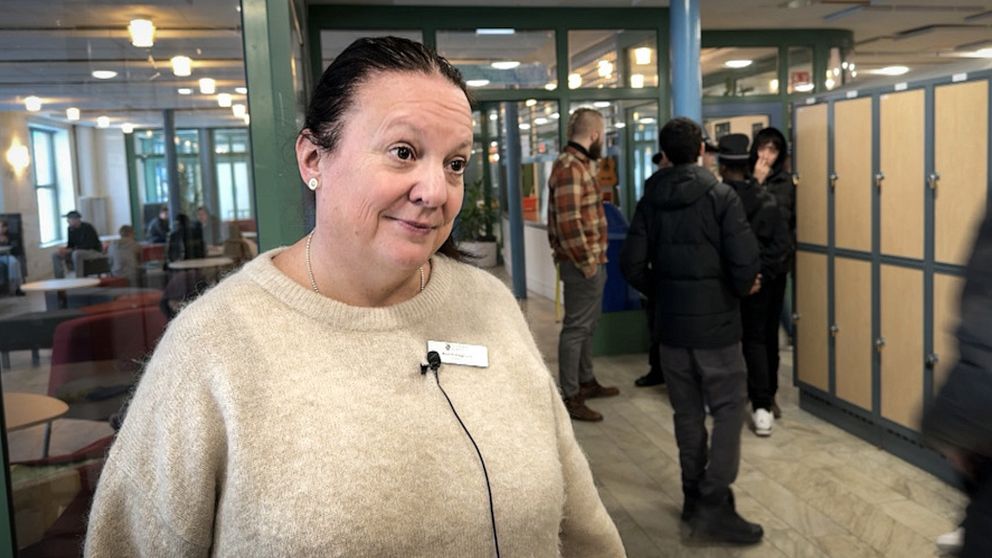 Rektorn på Kyrkskolan står inomhus vid några skåp. Bakom går elever förbi.