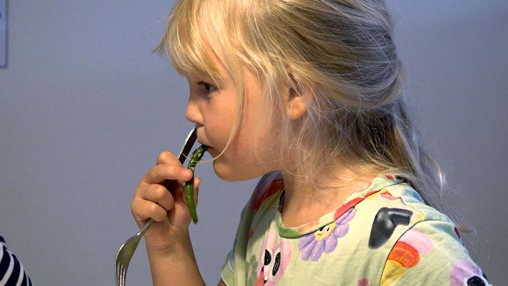 En flicka i profil som sitter och äter en grön böna.