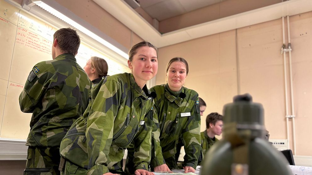 Värnpliktiga Moa Snitting Olcén och Ida Lindgren på Skydd C i Umeå lutar mot ett bord med en karta