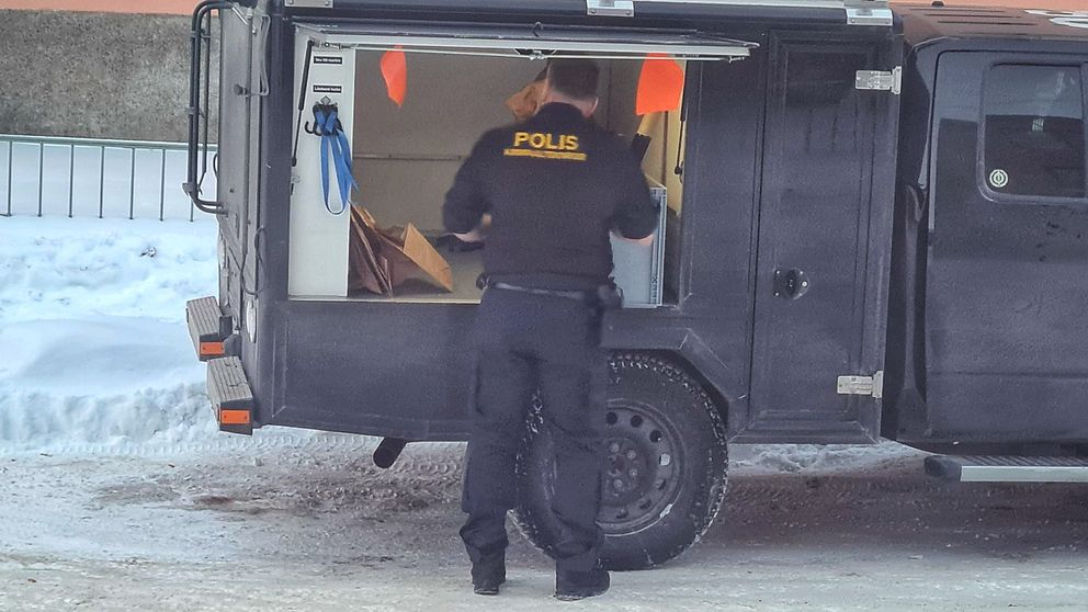 Polisens tekniker står  vid en svart teknikerbil.