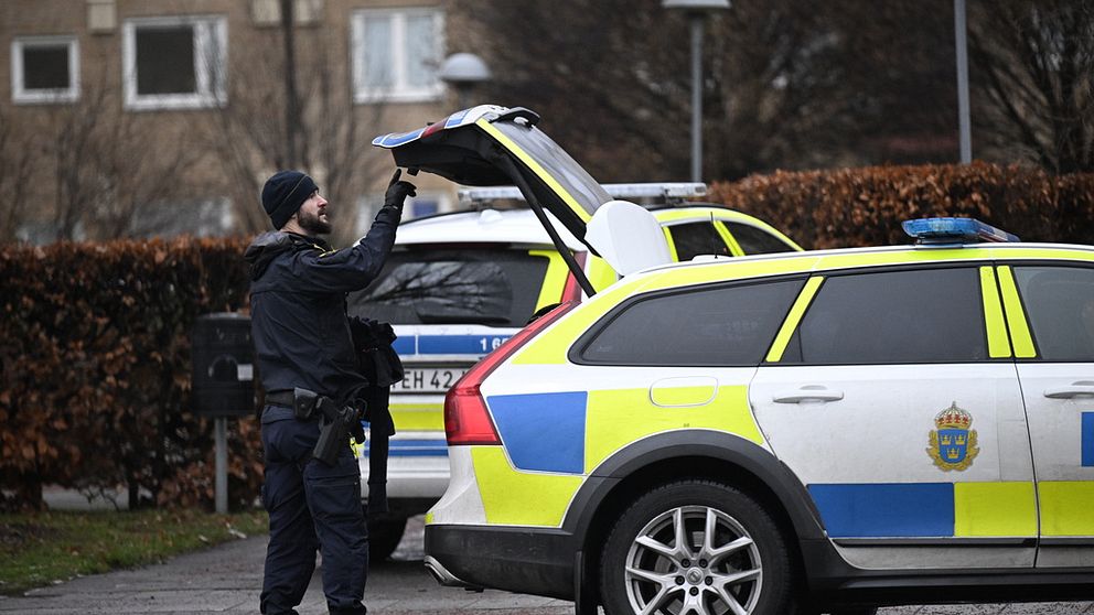 En polis står vid en polisbil med bagageluckan öppen.