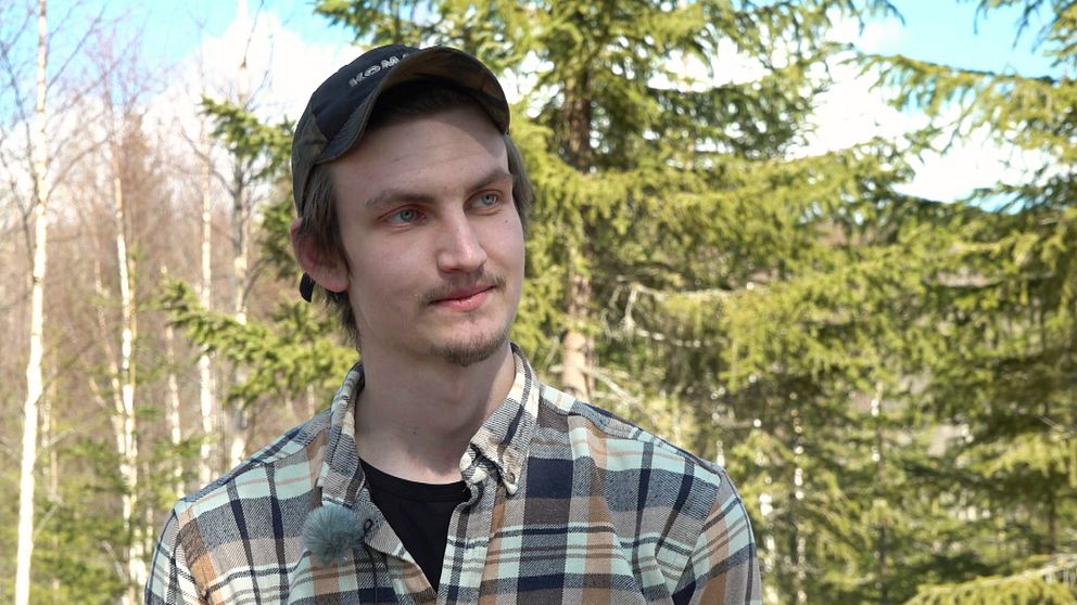 En man i 20-årsåldern med rutig skjorta som står i skogen vid Byberget i Ånge kommun.
