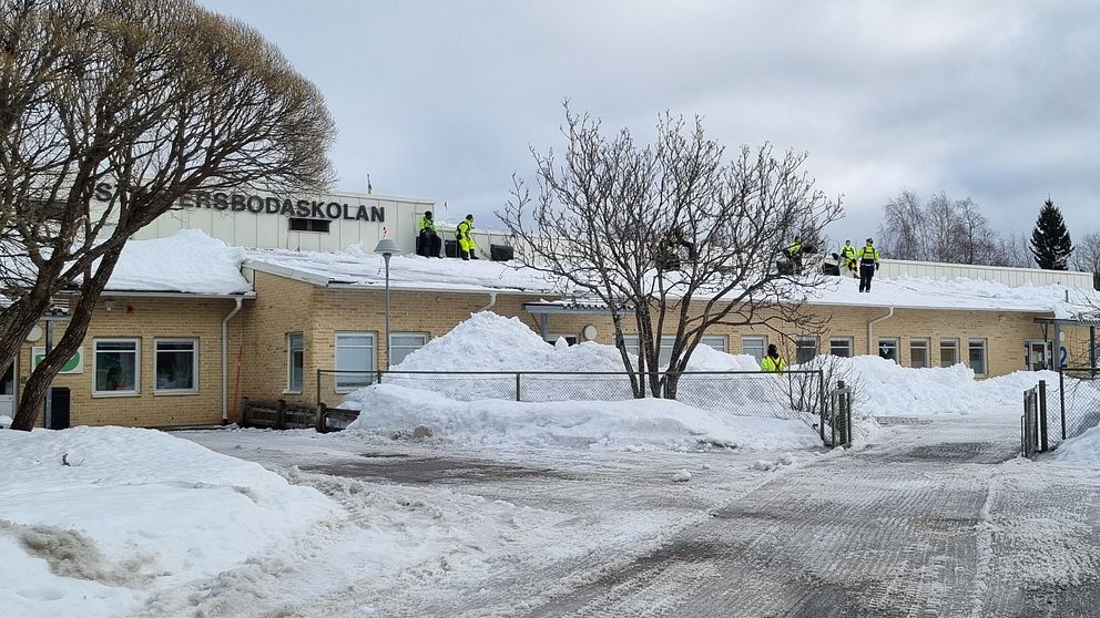 personer i varselkläder syns på taket på Östra Ersbodaskolan, snöhögar nedanför