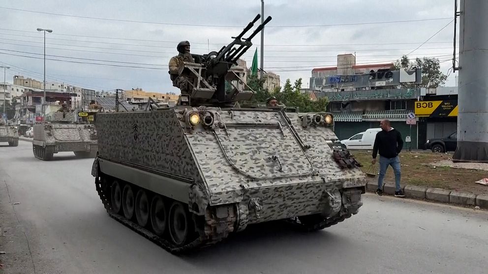 Militära fordon åker längs en gata, där en soldat på en kulspruteposition syns på toppen av fordonet.