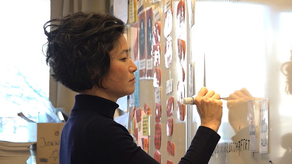 Helen Nilsson, ordförande i Sveriges Lärare i Halmstad, står framme vid whiteboardtavlan och skriver. I bakgrunden syns en bit av ett fönster och uppklistrade lappar på tavlan.