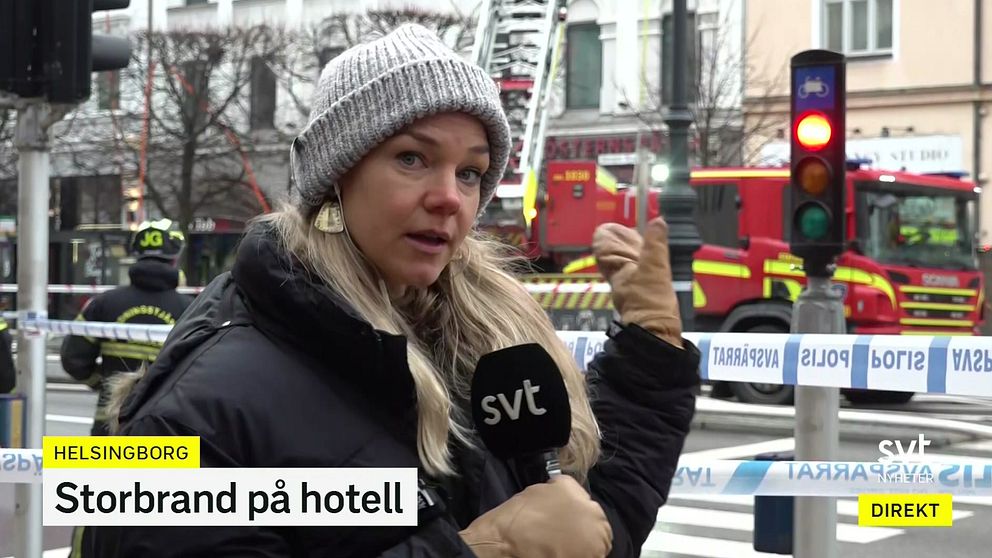 En reporter står i förgrunden och rapporterar om en storbrand på ett hotell i Helsingborg, med brandbilar och räddningstjänst synliga i bakgrunden. Trafikljus och avspärrningar är också synliga, vilket indikerar att området är stängt för allmänheten. Texten ”Storbrand på hotell” ingår i bilden.