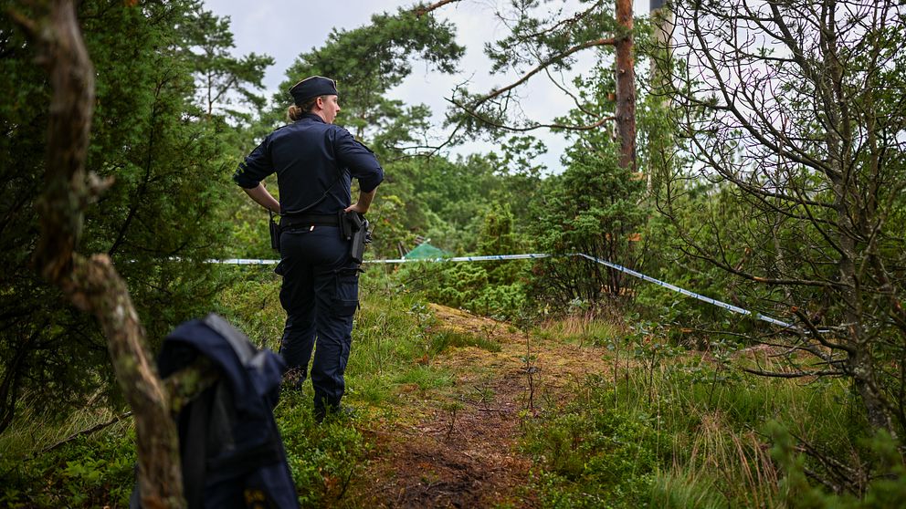 Poliskvinna står i en skogsglänta.