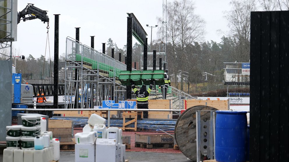 Byggarbetsplats med konstruktion av ställning och gröna metallramar. Maskiner och material runtom.