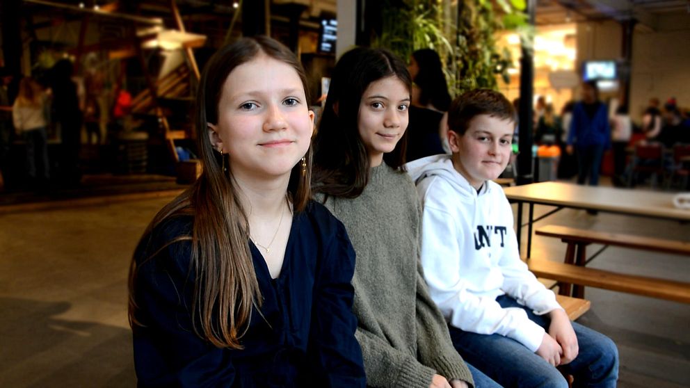 Tre skolelever personer sitter vid ett bord i en livlig inomhusmiljö, inne på Tom tits experiment i Södertälje.