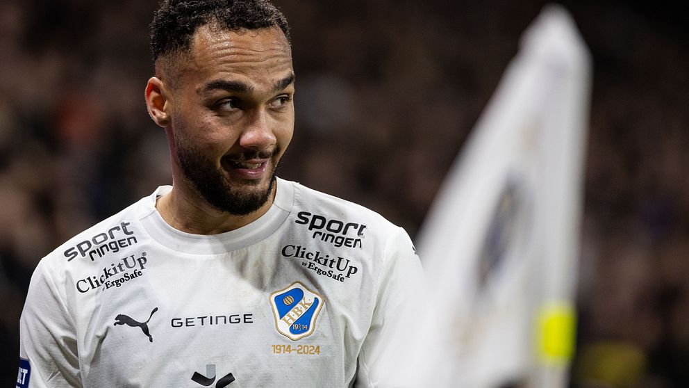 Fotbollsspelare i vit uniform vid hörnflagga på planen.