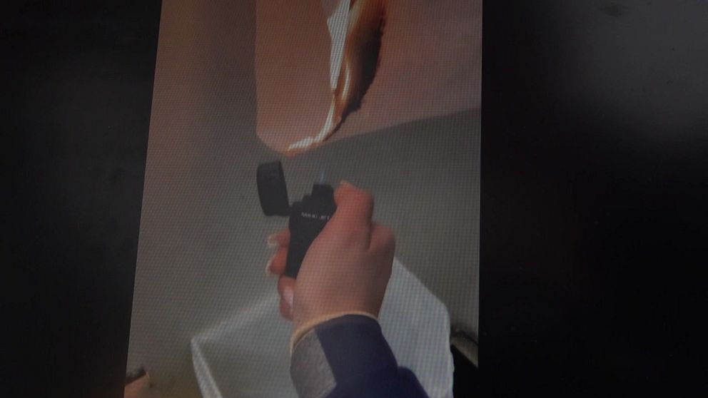 En hand håller en kamera riktad mot en vägg där en fiskbild projicerats. Bakgrunden är suddig och visar en modern inomhusmiljö.