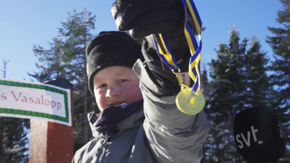 En liten pojke håller upp en medalj framför kameran som han vann i barnens vasalopp.