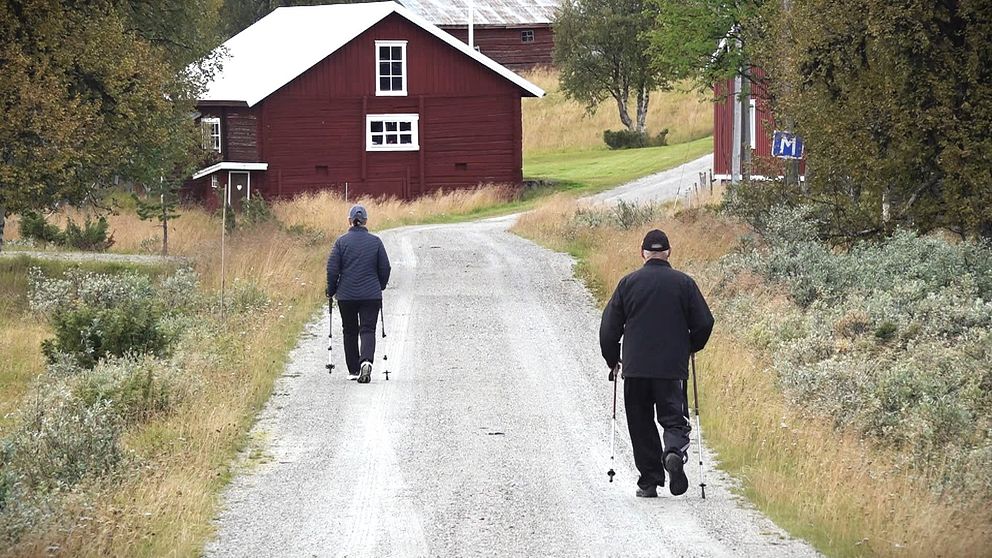 Två äldre människor går längs den enskilda vägen genom byn Högvålen i Härjedalen