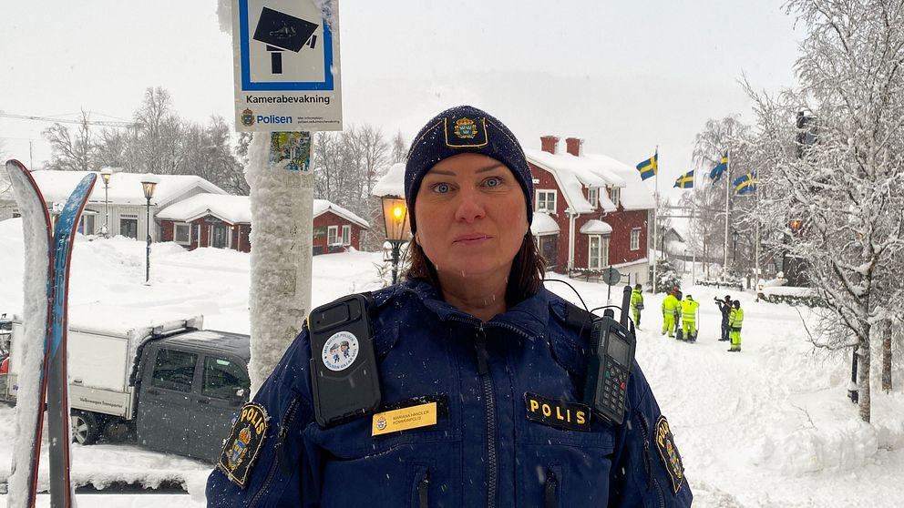 Kommunpolisen Mariana Handler står i Åre med Åre torg i bakgrunden. En skylt som indikerar kameraövervakning sitter på en stolpe. ä
