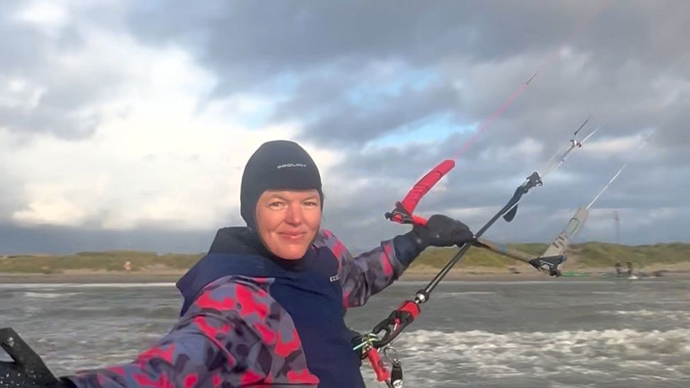 Person i färgglad jacka kitesurfar vid en stormig kust under molnig himmel.