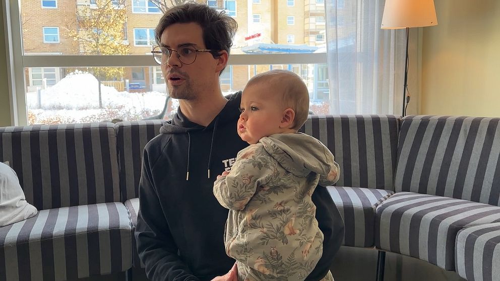 En man med glasögon sitter på golvet med ett barn i knäet.