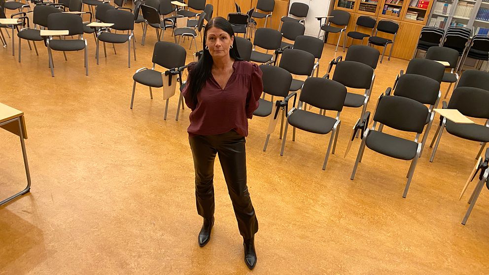 Kvinna står i skolas aula framför rader med stolar