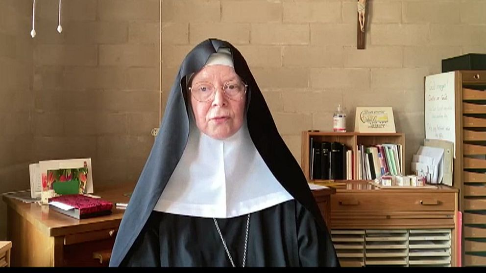 Nunna i svart och vitt klädesplagg sitter i ett kontor med böcker och skrivbord.