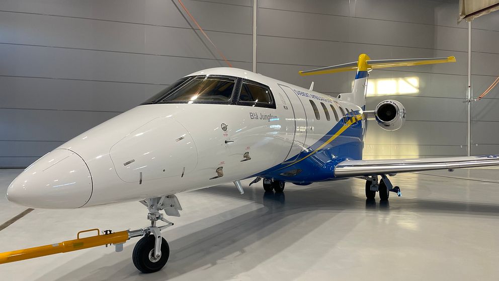 Ett av Svenskt Ambulansflygs flygplan i en hangar. Planet är vitt med blå och gula detaljer.