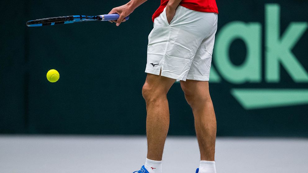 En man som studsar en tennisboll mot marken med sitt tennisrack.