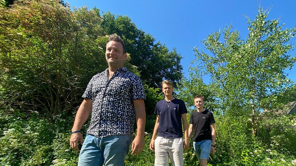 Tre bandmedlemmar från dansbandet Donnez går över en gräsmatta en solig sommardag.