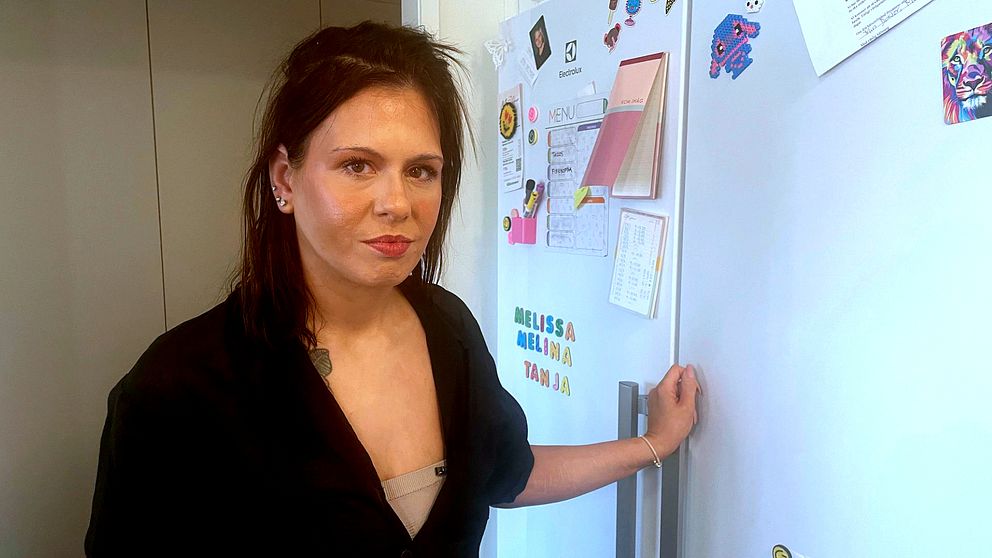 Person vid kylskåp, prydd med magnetiska lappar och teckningar.