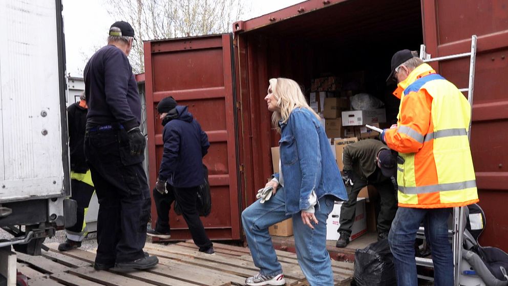 flera personer står vid en container och en kvinna tittar in i ett lastbilsflak.