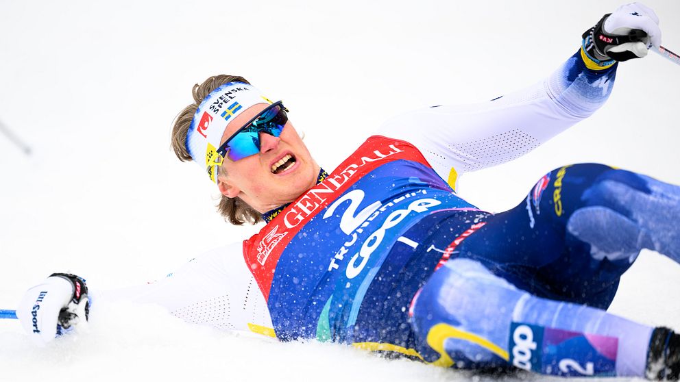 Skidåkare i målområdet, liggande på snön, iförd tävlingsdräkt och startnummer två.