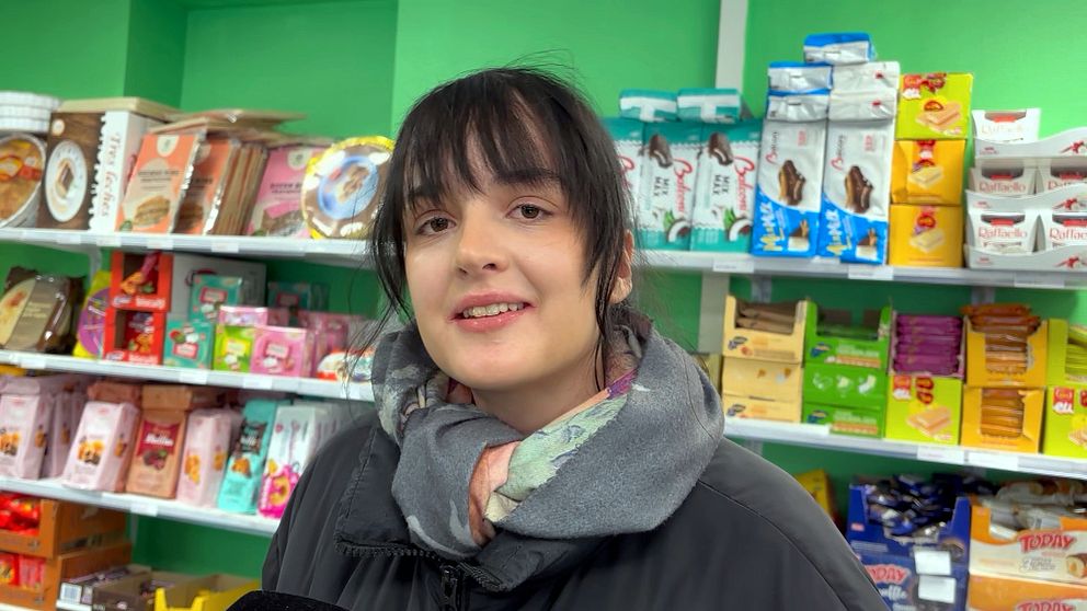 Person i en butik, omgiven av diverse matvaror på hyllor.