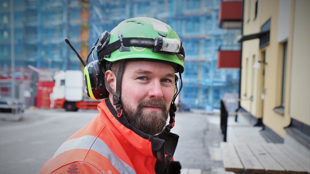 Man i byggnadskläder sitter på en bänk framför ett hus.