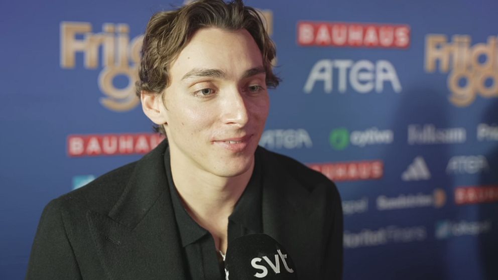 En man i en svart jacka intervjuas på en röd matta vid en eventpremiär, omgiven av en blå vägg med sponsormärken och logotyper. Han håller en mikrofon med SVT:s logotyp.