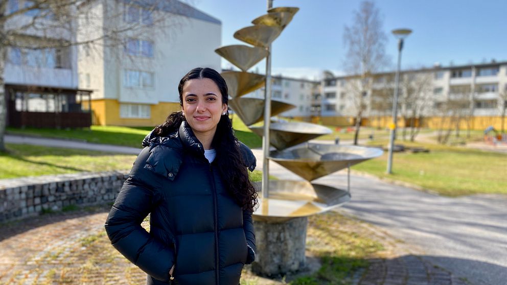 En kvinna, klädd i svart, står i ett bostadsområde