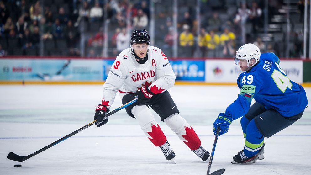 Ishockeymatch mellan Kanada och Slovenien, två spelare kämpar om pucken på isen.