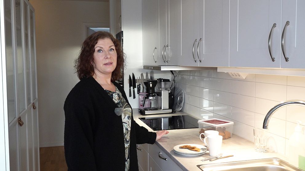 På bilden syns Marianne Kjellberg som står i familjens kök. Hon tittar mot kameran och har ena handen på köksbänken där det står tallrikar, pepparkakor och muggar.