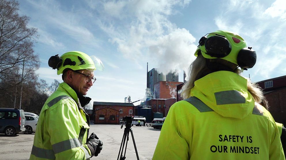 Två personer i ljusgrön varselklädsel och hjälmar vid Aspa bruk utanför Askersund, pratar om utsläpp från fabriken.