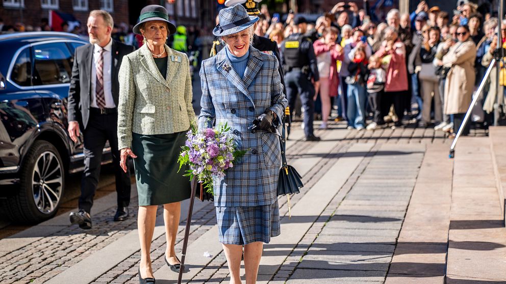Drottning Margrethe går med blombukett framför publik på en solig gata.