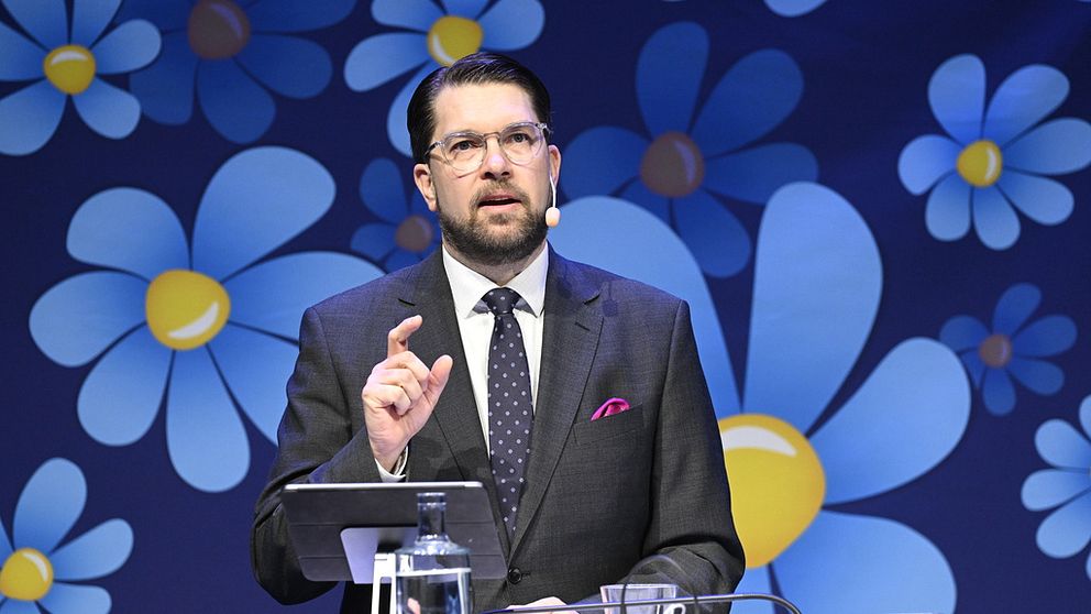 Åkesson framför en fondvägg täckt av blommor.