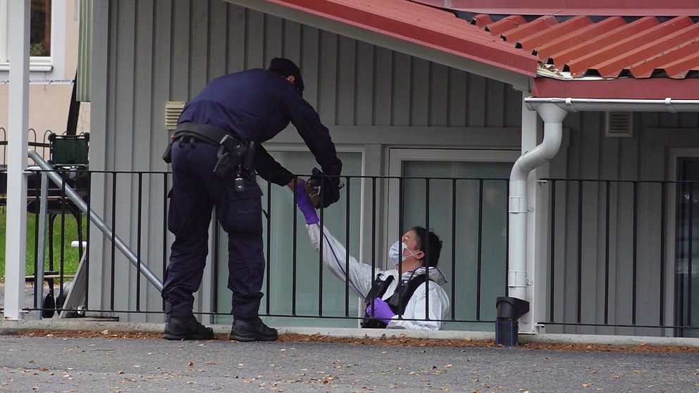 En polis och en tekniker står i en trapp och räcker något till varandra