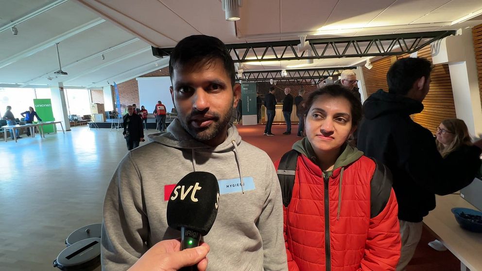 En man och en kvinna intervjuas av SVT i en inomhusmiljö med människor i bakgrunden