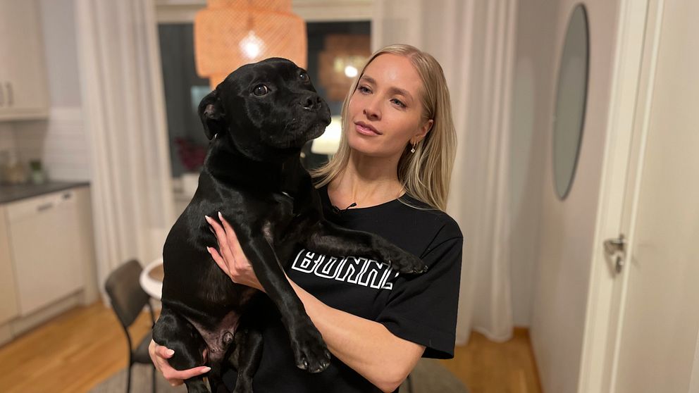Kvinna håller i en svart hund i sitt hem.
