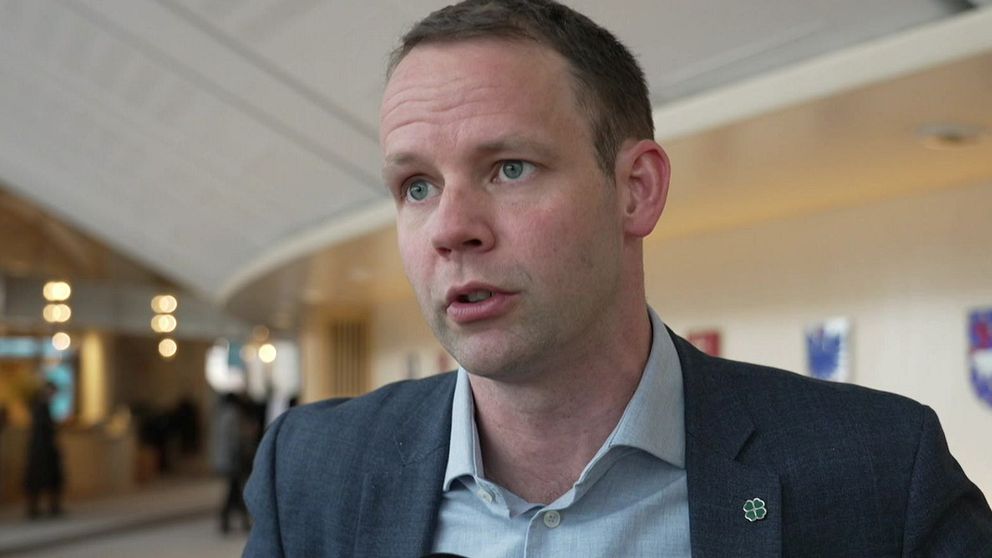 Reporter håller SVT-mikrofon i ett offentligt utrymme. Logotypen för Rapport syns.