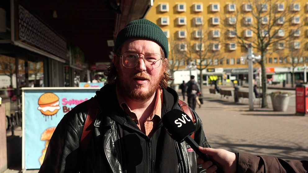 SVT intervjuar person på gata, orange byggnad i bakgrunden.