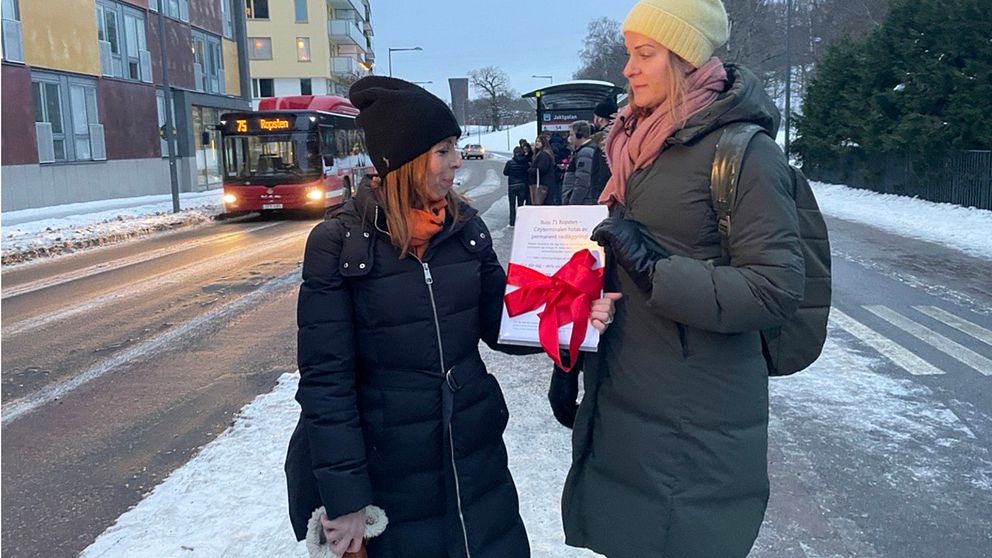 Två resenärer håller i en protestlista framför en busshållplats och en buss.