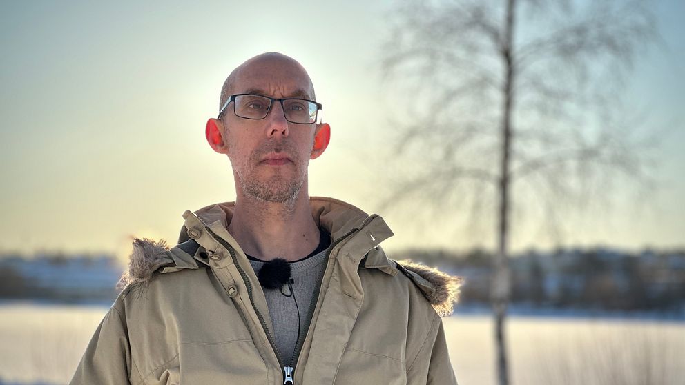 Man i täckjacka står i motljus vid Lillfjärden, Hudiksvall.