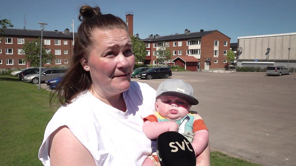 Mamma i vit t-shirt och bebis med keps i famnen – i Munkfors i Värmland som är en plats i Sverige där föräldrar tar ut minst föräldraledighet.
