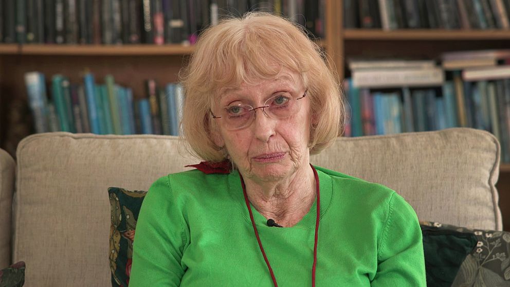 Ulla, en kvinna i grön tröja, sitter framför bokhyllor och berättar om hur hon själv betalat över 300 000 kronor för att åka till USA och ta ut den slynga som opererades in i hennes underliv mot kontinensbesvär.