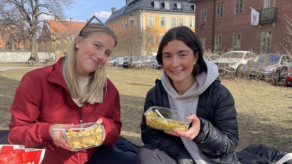 Två personer sitter på gräs och äter intill Stockholms nation.