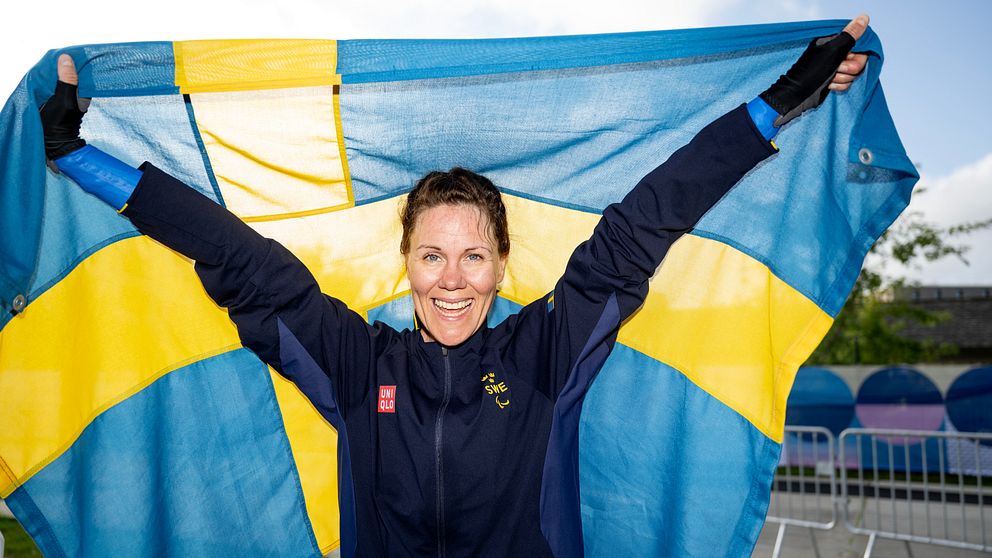 Paracyklisten Anna Beck håller stolt upp svensk flagga bakom sig.