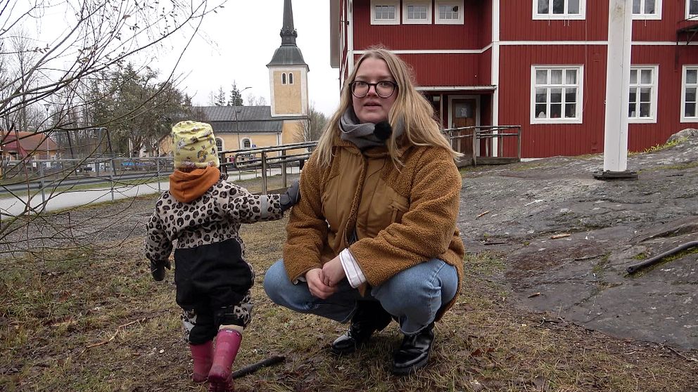 En förälder sitter på huk framför Himmeta skola på landsbygden utanför Köping. Bredvid står ett barn i förskoleålder.